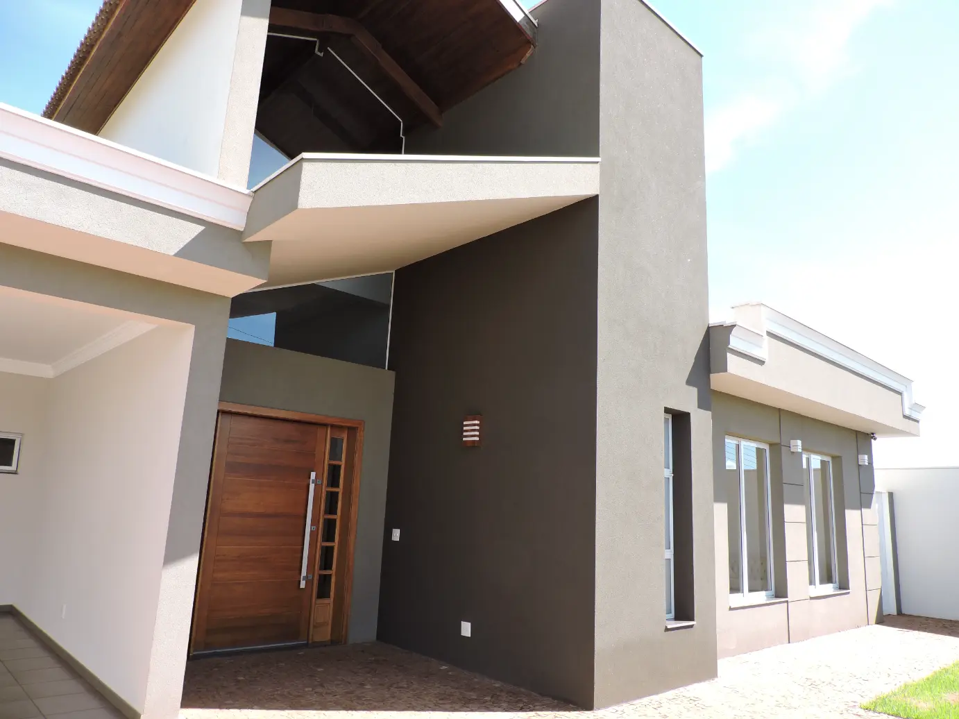 Fachada residencial contemporânea com pé-direito alto e porta de madeira